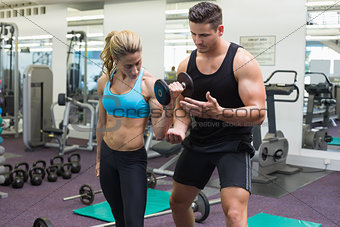 Personal trainer coaching female bodybuilder lifting dumbbell