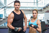 Bodybuilding man and woman holding dumbbells smiling at camera