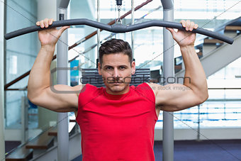 Handsome bodybuilder using weight machine for arms
