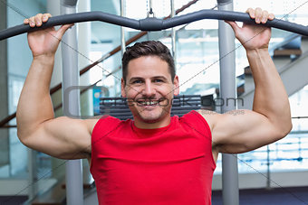 Handsome smiling bodybuilder using weight machine for arms
