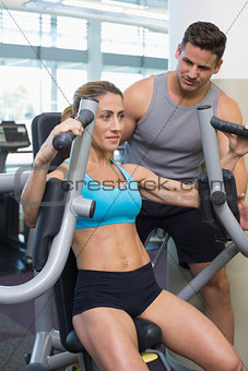 Personal trainer coaching smiling female bodybuilder using weight machine