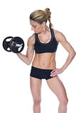 Female bodybuilder holding large black dumbbell with arm up looking at bicep