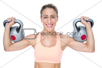 Happy female crossfitter lifting kettlebells looking at camera