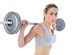 Strong female crossfitter lifting barbell behind head looking at camera