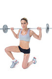 Strong female crossfitter lifting barbell behind head looking at camera