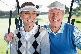 Happy golfing couple sitting in golf buggy smiling at camera
