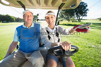 Happy golfing couple sitting in golf buggy