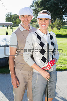Happy golfing couple looking at camera with golf buggy behind
