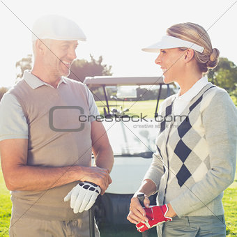 Happy golfing couple chatting with golf buggy behind