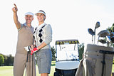 Happy golfing couple pointing with golf buggy behind