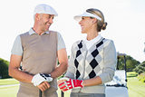 Happy golfing couple facing each other with golf buggy behind