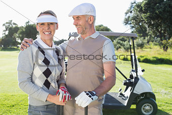 Happy golfing couple with golf buggy behind