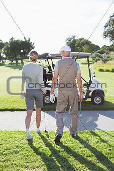 Happy golfing couple walking towards the buggy