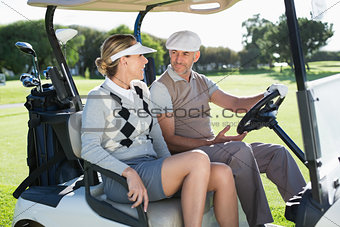 Happy golfing couple sitting in buggy smiling at each other
