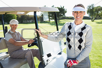 Happy golfing couple smiling at camera with their buggy
