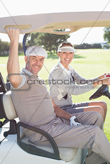 Happy golfing couple smiling at camera in their buggy