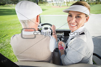 Golfing couple driving in their golf buggy with woman smiling at camera