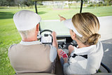 Golfing couple driving in their golf buggy with woman pointing