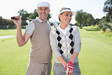 Golfing couple smiling and holding clubs