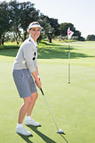 Lady golfer on the putting green at the eighteenth hole smiling at camera