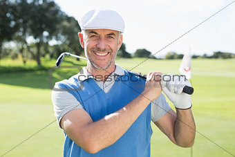 Golfer standing and swinging his club smiling at camera