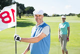 Happy golfer holding eighteenth hole flag with partner behind him