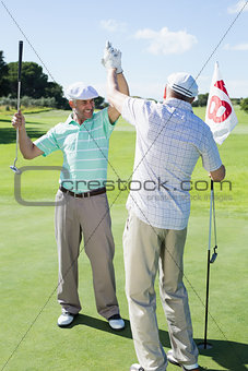 Golfing friends high fiving on the eighteenth hole