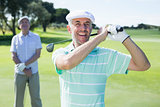 Golfer swinging his club with friend behind him