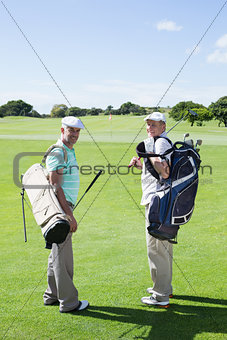Golfer friends smiling at camera holding their golf bags