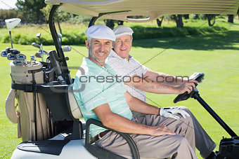 Golfing friends smiling at camera in their golf buggy