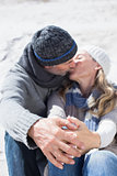 Attractive couple kissing on the beach in warm clothing