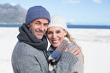 Attractive couple smiling at camera on the beach in warm clothing