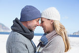 Attractive couple smiling at each other on the beach in warm clothing