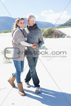 Smiling couple strolling on the beach in warm clothing