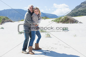 Smiling couple hugging on the beach in warm clothing