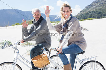 Carefree couple going on a bike ride on the beach waving at camera
