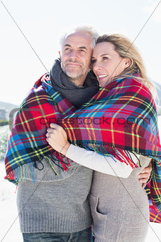 Happy couple wrapped up in blanket standing on the beach