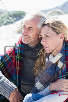 Happy couple wrapped up in blanket sitting on the beach