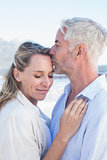 Man kissing his smiling partner on the forehead at the beach