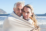 Smiling couple wrapped up in blanket on the beach