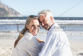 Couple sitting on the beach under blanket smiling at camera
