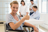 Casual businesswoman in wheelchair smiling at camera with team behind her