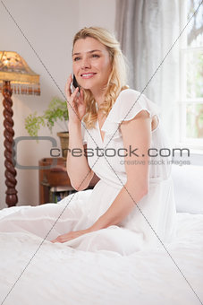 Pretty blonde sitting on bed talking on the phone