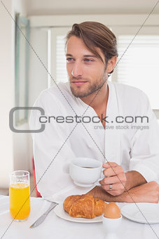 Handsome man having breakfast in his bathrobe drinking coffee