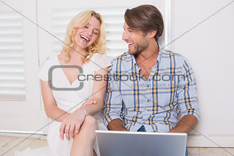 Happy couple sitting on floor using laptop