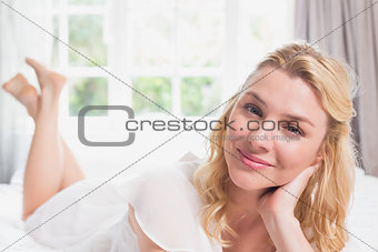 Pretty blonde lying on bed smiling at camera