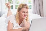 Pretty blonde lying on bed using laptop