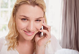 Pretty blonde sitting on bed on the phone smiling at camera