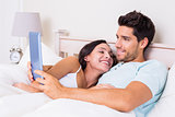 Attractive couple lying in bed with tablet pc