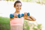Fit woman exercising with dumbbells in the park